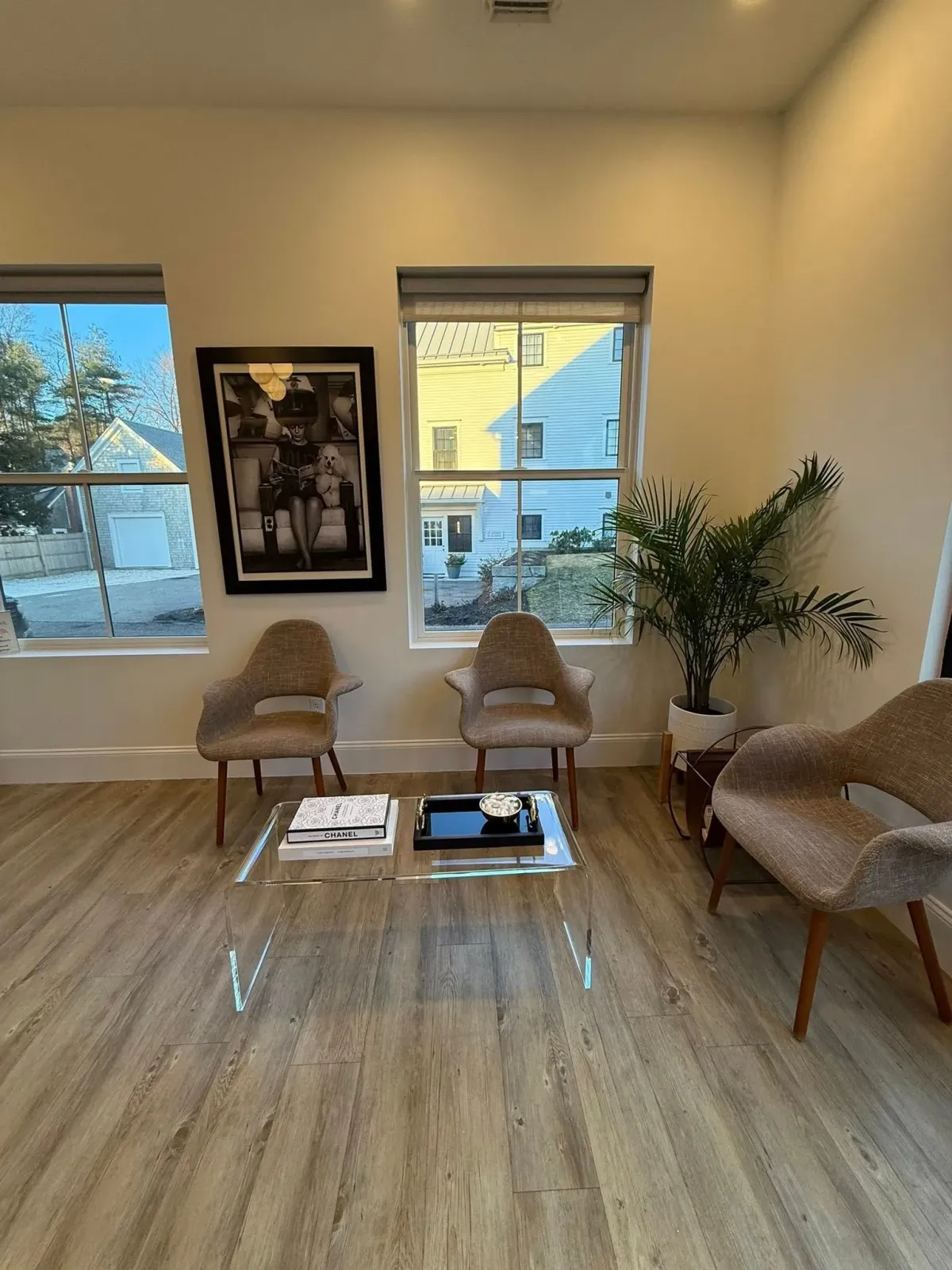 Bright waiting room with wicker chairs, coffee table, framed art, and two windows overlooking greenery