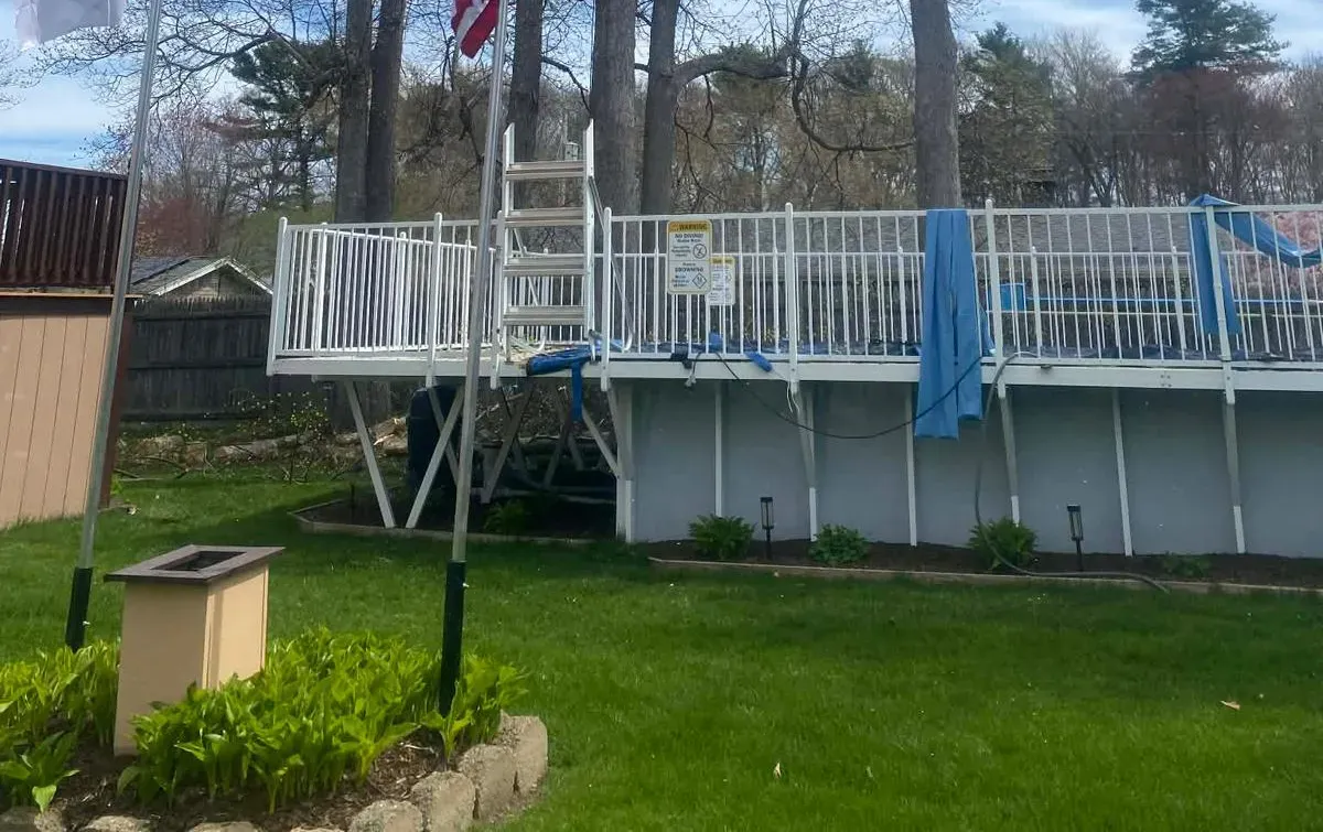 Backyard deck with white railing and ladder, green lawn below, and a blue towel draped over the fence