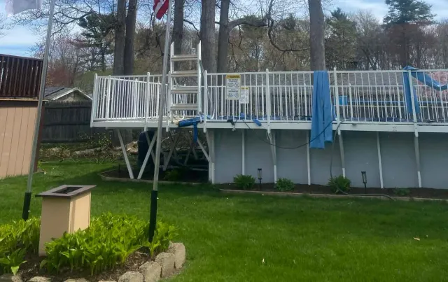 Backyard deck with white railing and ladder, green lawn below, and a blue towel draped over the fence