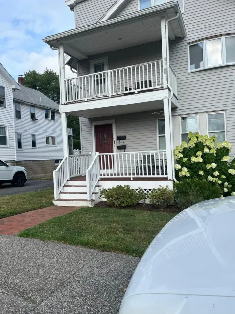 Two-story gray townhouse with white trim, red front door, and porch, seen from the driveway.