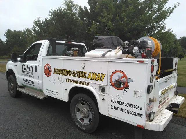 White utility truck with equipment and recycling decals parked on a roadside, trees in the background