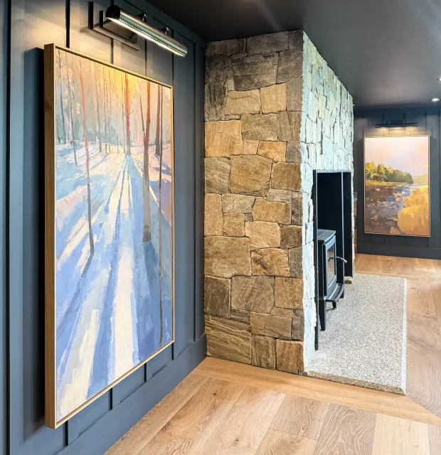 Hardwood floor installation in a Duxbury living room with blue walls, a stone fireplace, and forest landscape artwork.
