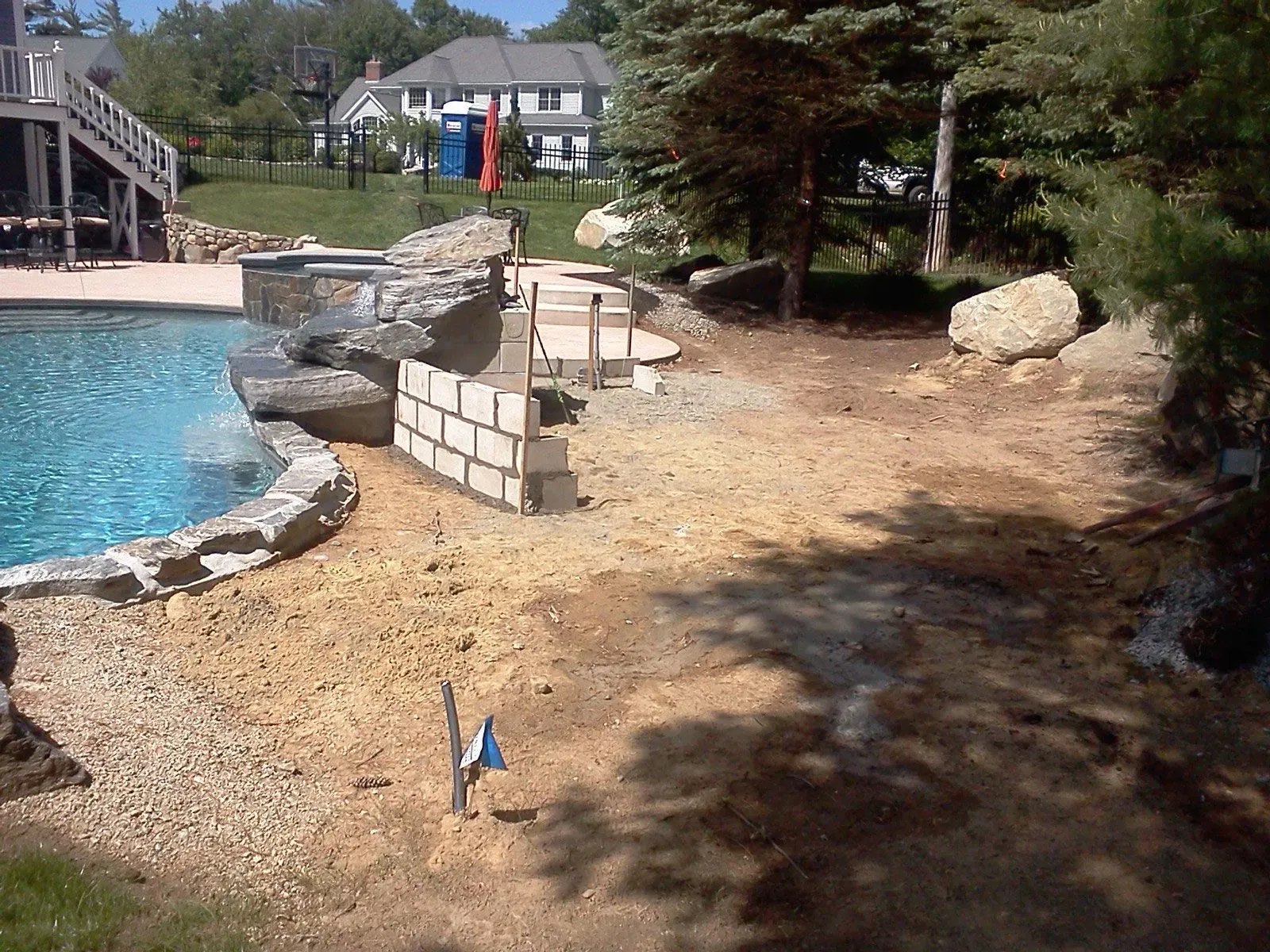 Backyard pool with stone border, patio chairs, and a house in the background
