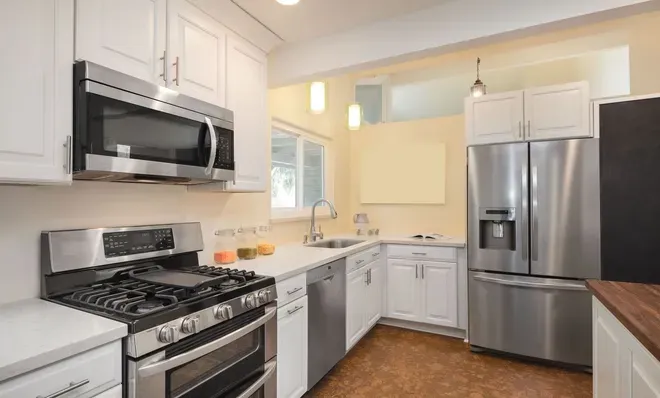 A modern kitchen with white cabinets, stainless steel appliances, a gas stove, and light countertops.
