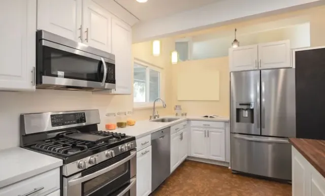 A modern kitchen with white cabinets, stainless steel appliances, a gas stove, and light countertops.