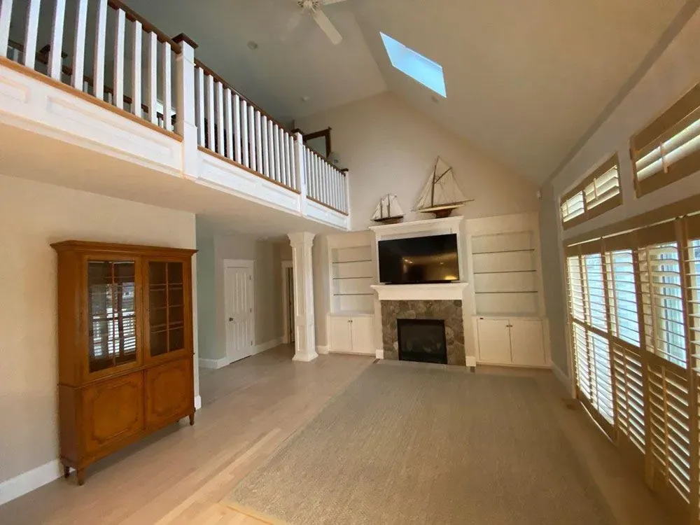 Spacious living room with vaulted ceiling, loft railing, fireplace, and large windows with shutters