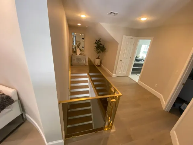 Hallway with stairs and gold railing, light wood floors, neutral walls, and recessed lighting.