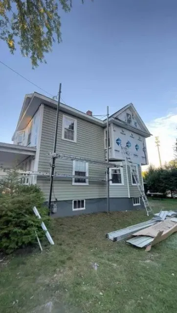 House exterior with scaffolding and construction materials in a grassy yard under a clear sky