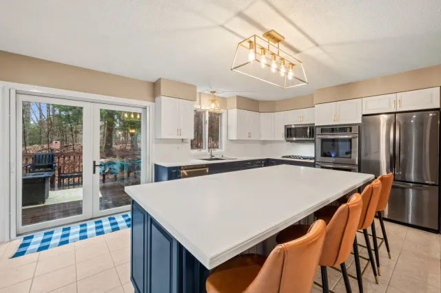 A modern kitchen with a large navy blue island, white countertops, stainless steel appliances, and brown bar stools.