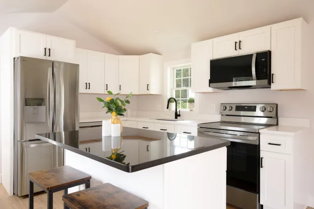 Modern kitchen with white cabinets, black countertops, stainless steel appliances, window with greenery outside, and a decorated kitchen island.