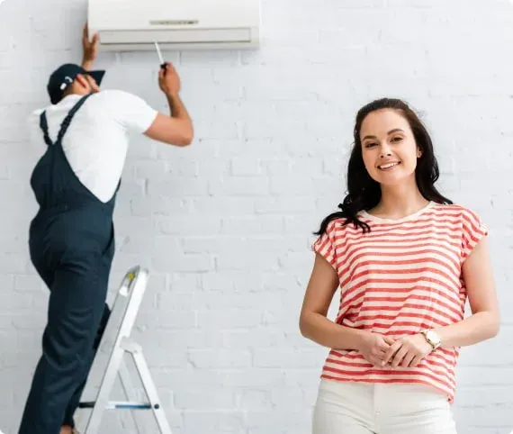 Smiling customer with a technician installing an air conditioner in the background
