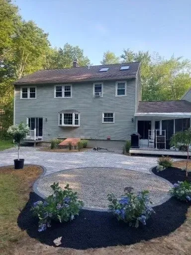A two-story light gray house with a new gravel patio and landscaping beds featuring hydrangea bushes in the backyard.