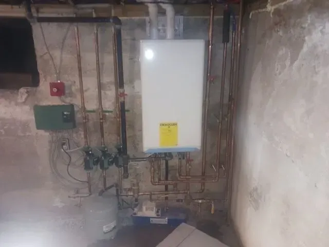 A water heater is sitting in a basement next to a wall.
