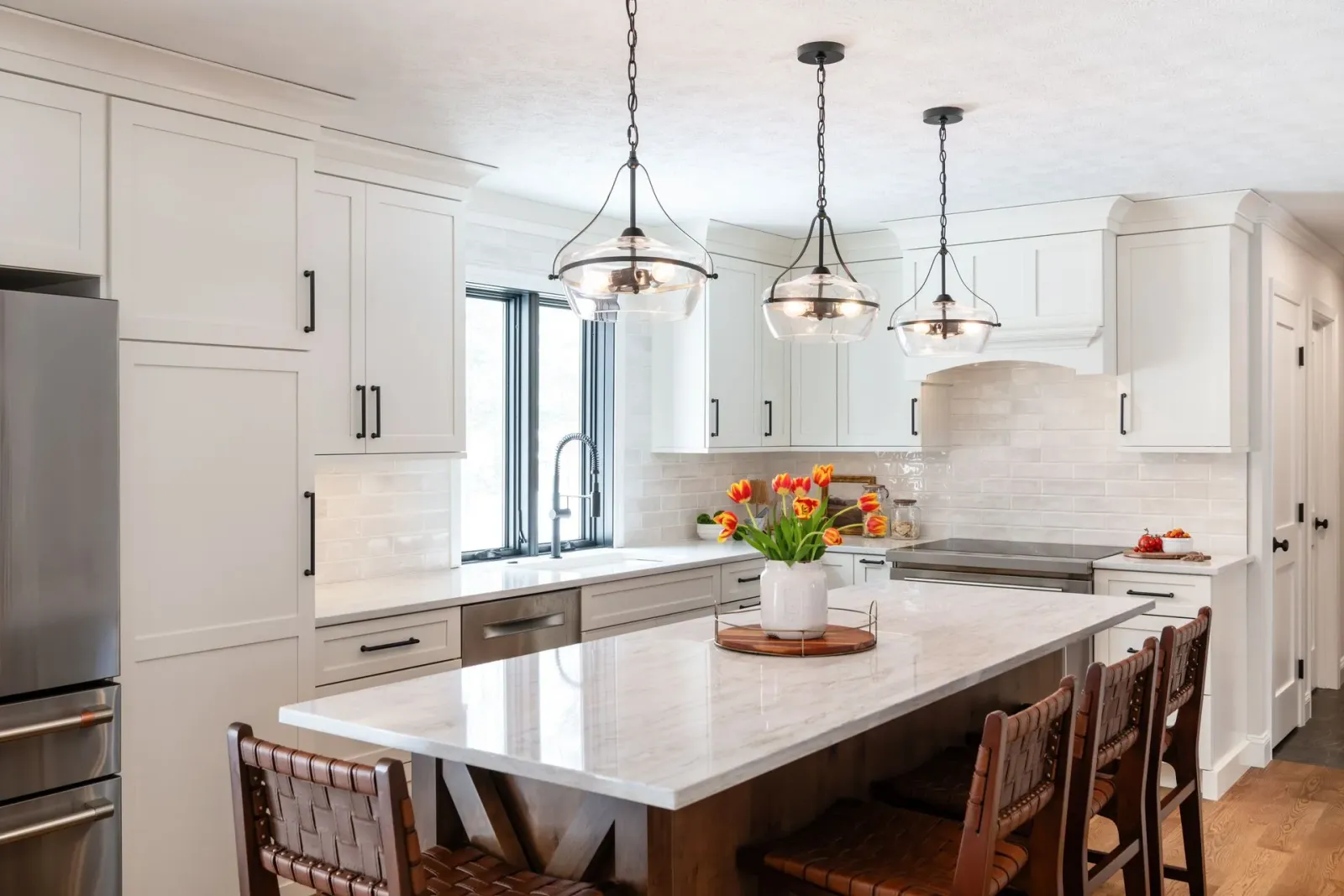 Bright white kitchen with island, pendant lights, marble counters, and a vase of orange flowers