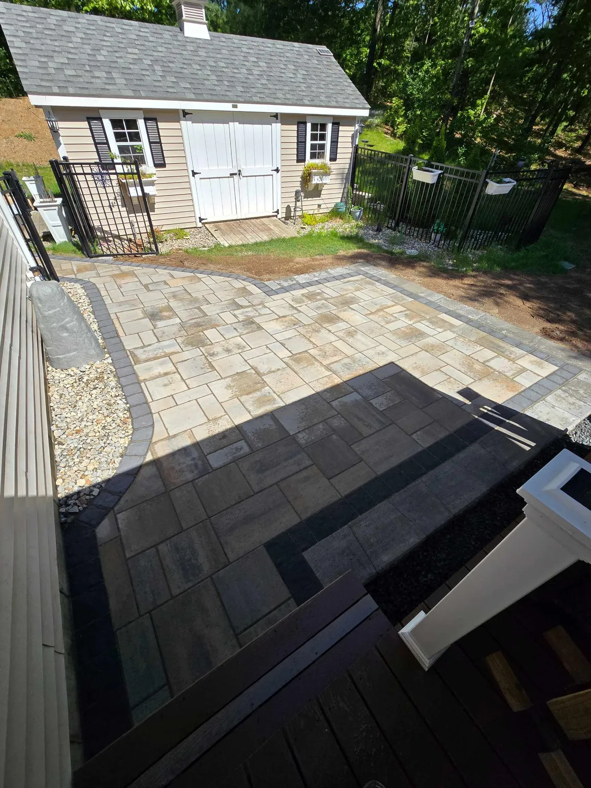 A residential backyard shows a freshly dug trench along a marked garden area with a yellow-handled shovel.