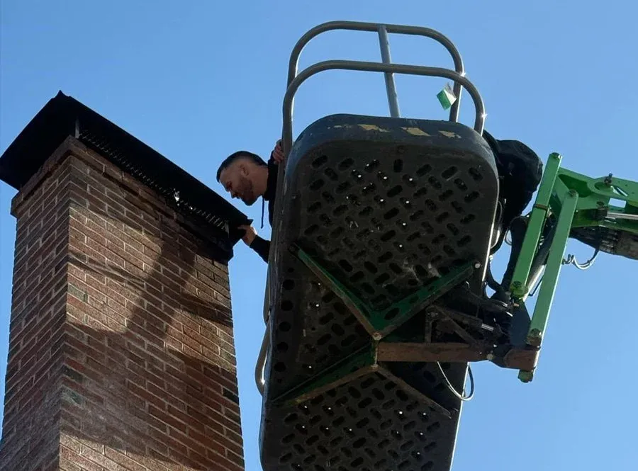 A worker on a lift inspecting or repairing a chimney on a brick building during daytime.