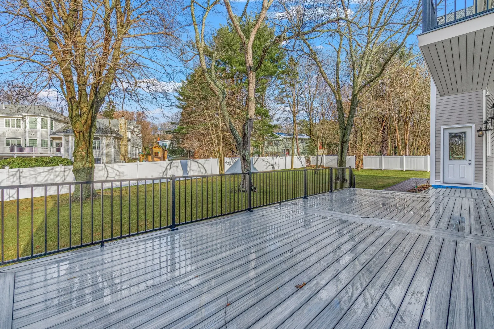 Backyard with a wooden deck, green grass, trees, and a white fence surrounding the yard.