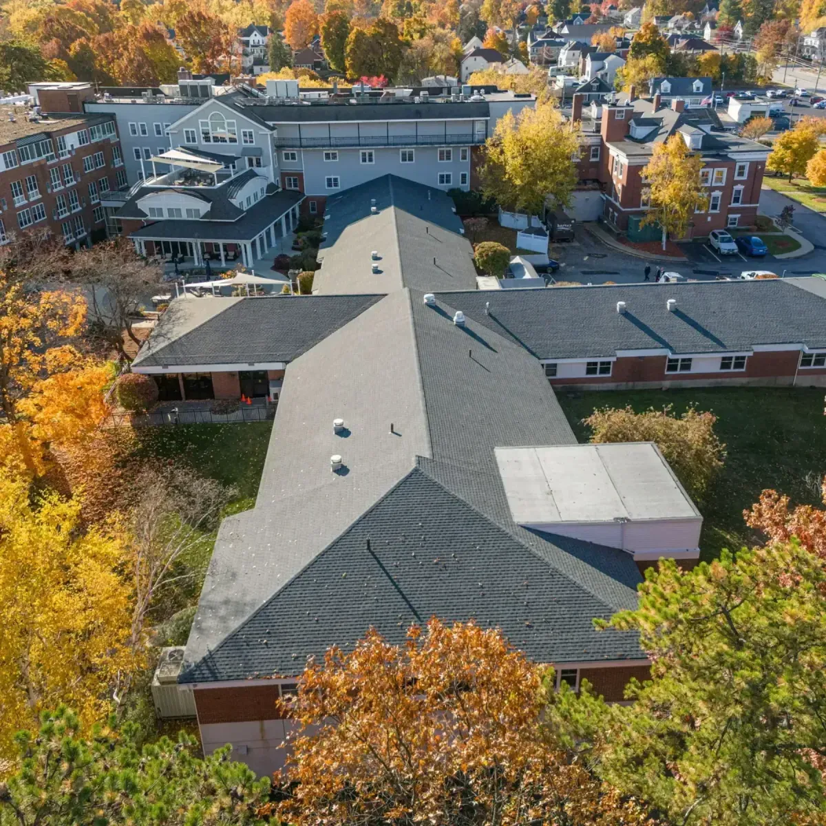 Aerial view of a commercial building with a newly installed asphalt shingle roof surrounded by autumn foliage, showcasing Crown Roofing's expertise in roofing solutions for businesses.