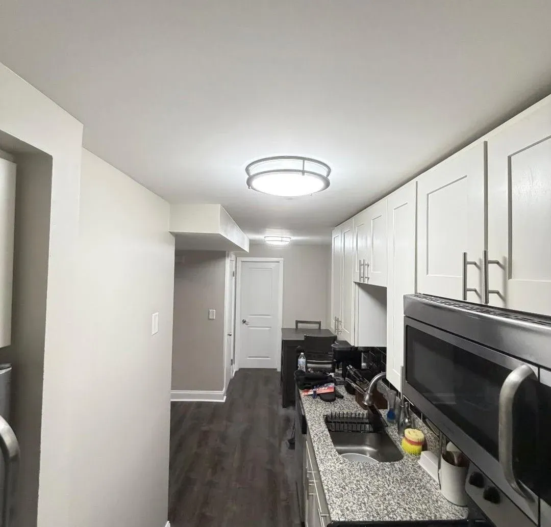 Modern kitchen with white cabinets, granite counter, dark floor, and stainless steel appliances.