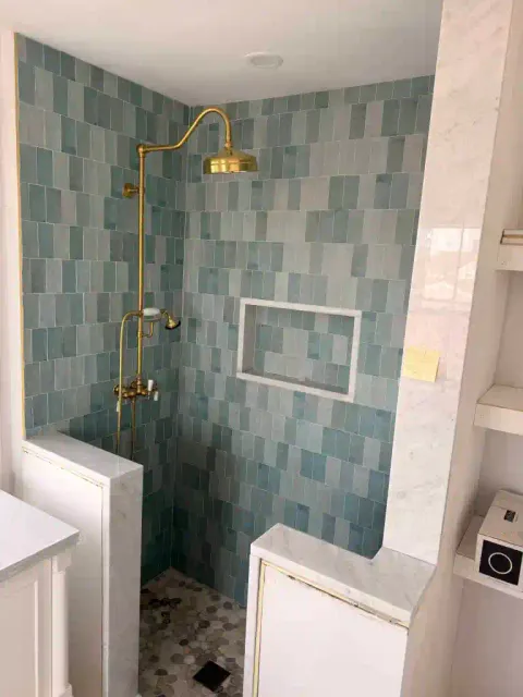 Contemporary shower with gold fixtures and blue tile walls.
