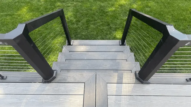 View of outdoor wooden stairs with black railings leading down onto a grassy lawn.