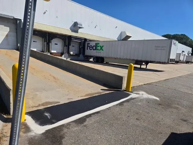 FedEx trailer at a loading dock with a ramp and yellow bollard under a blue sky