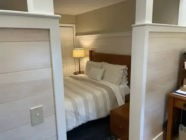 Cozy bedroom with partial wall divider, neutral tones, and built-in wood accents