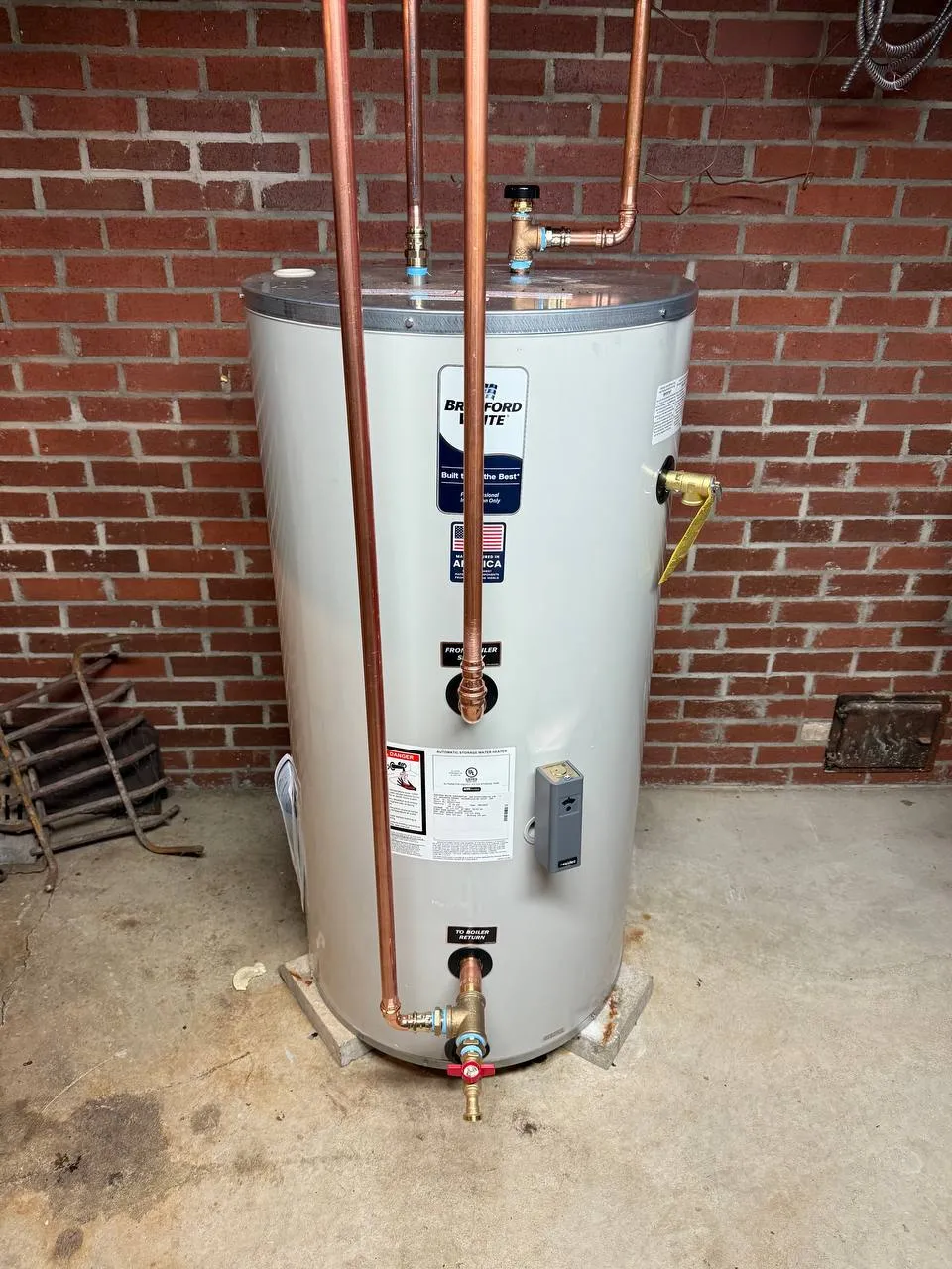 Indirect water heater with copper riser pipes and shut-off valves against a brick wall