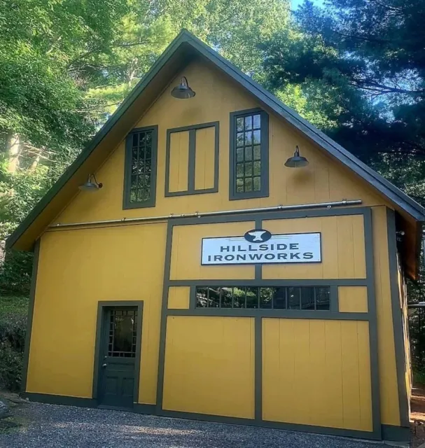 Yellow barn with black trim and a sign reading 'Hillside Iron Works'.