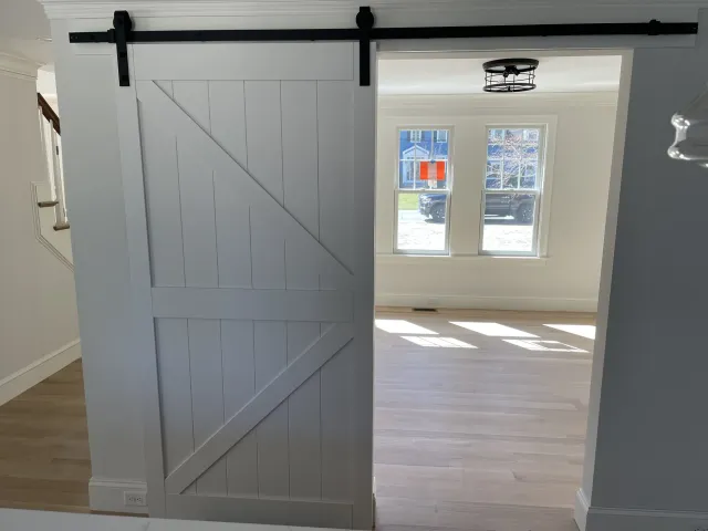 White sliding barn door partially open, revealing a bright room with large windows and wooden flooring.