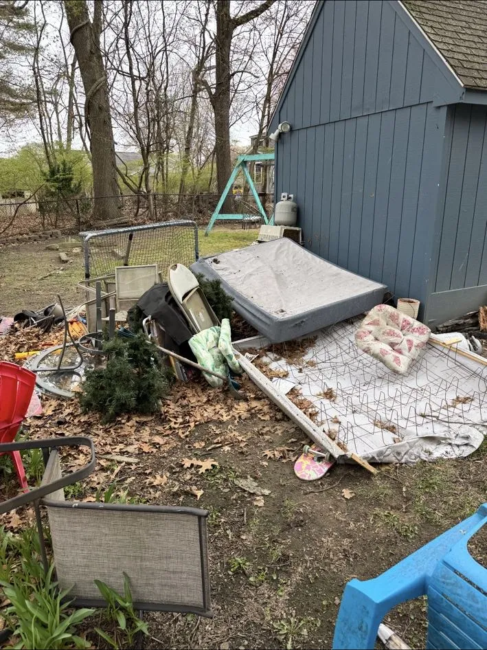 Same yard before, piled with a mattress, patio furniture and debris