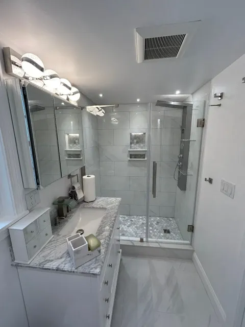 Modern bathroom with white and gray tile, glass shower, vanity, and overhead lighting.