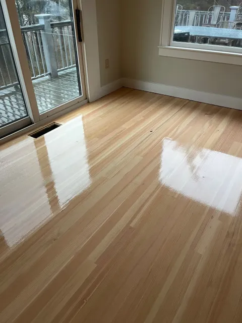 Shiny, light-colored wood floor partially covered with white substance, next to a sliding door leading to a deck.