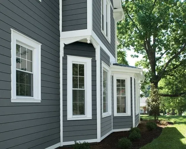 Modern gray and white house exterior with large windows and manicured landscaping on a sunny day