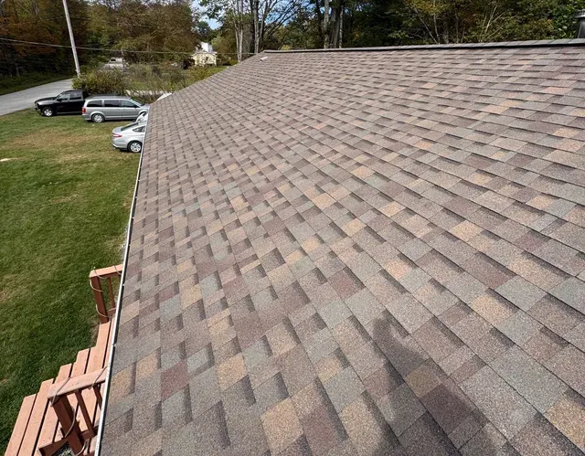 Shingled roof viewed from above, with a lawn, parked cars, and trees in the background.