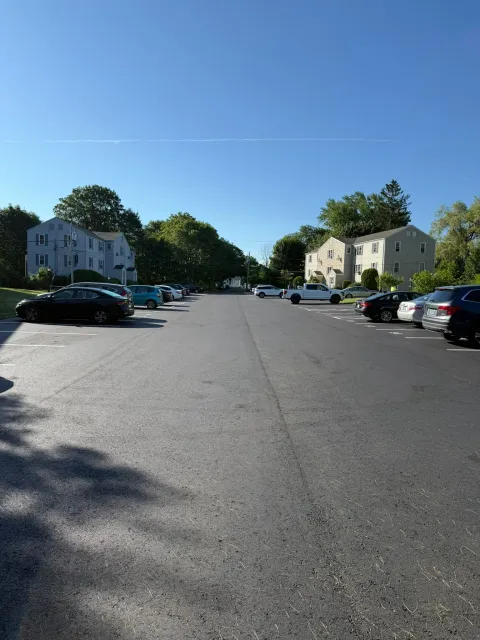 Parking lot between two apartment buildings on a clear day with several parked cars.