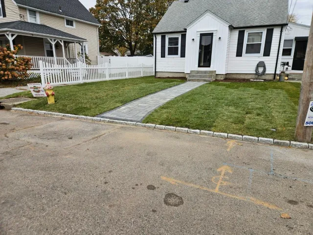 A small white house with a stone pathway and green lawn, viewed from the street.