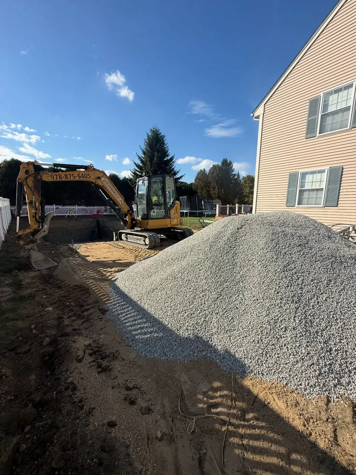 Excavator next to a house with a pile of gravel. Construction site with blue sky.