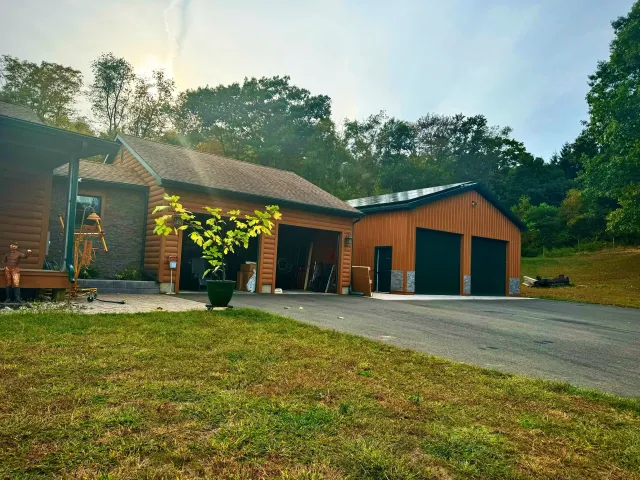 A log cabin-style house with an attached garage and a metal roof outbuilding, surrounded by trees.