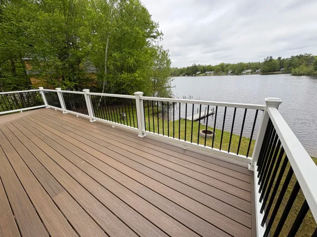 A wooden deck overlooking a body of water with trees and houses in the background.