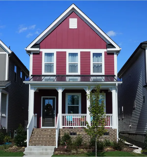 A two-story residential house, painted in a vibrant red, with a welcoming main entrance and a well-kept front garden featuring a leafy tree, adding a natural and homely touch.