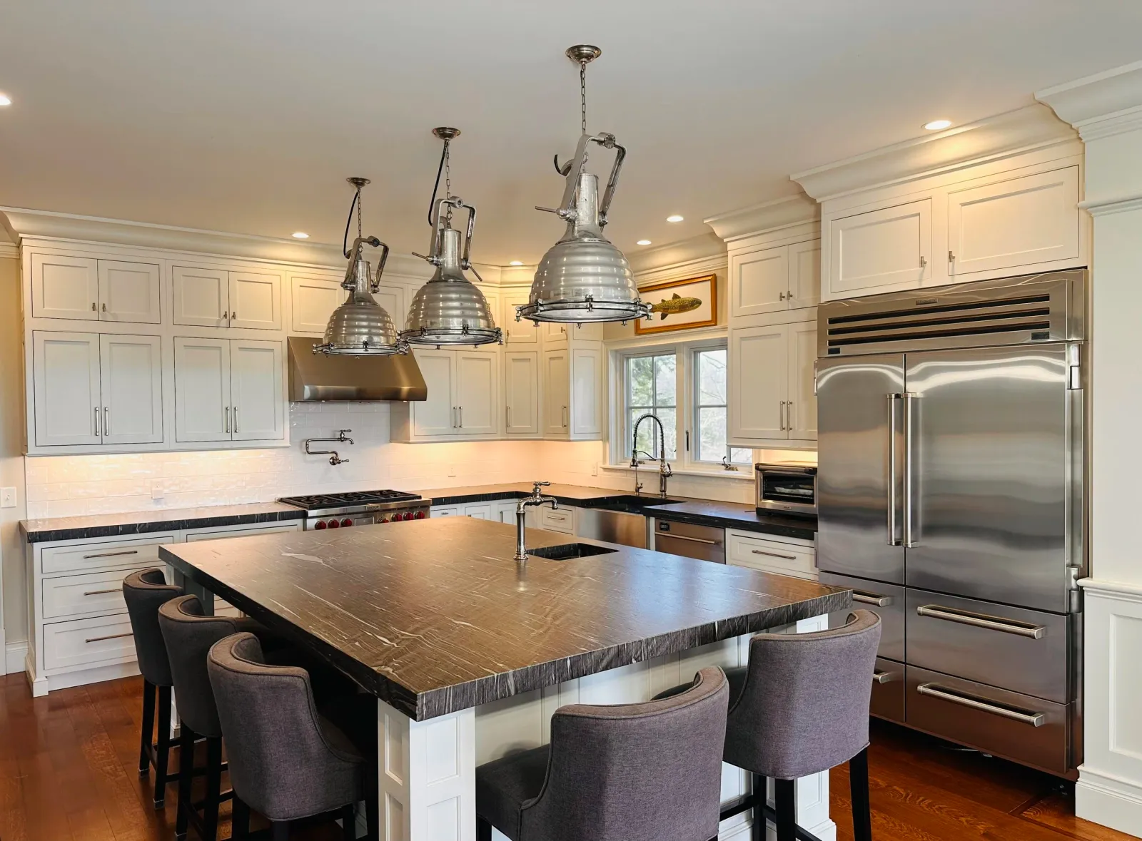 Modern kitchen with white cabinetry, stainless steel appliances, a large wooden island with seating, and industrial-style pendant lights.