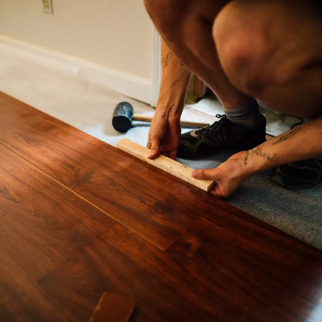 Worker kneeling to fit a dark hardwood plank into place with a tapping block and mallet