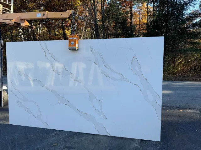 A large white granite slab is being lifted by a crane.