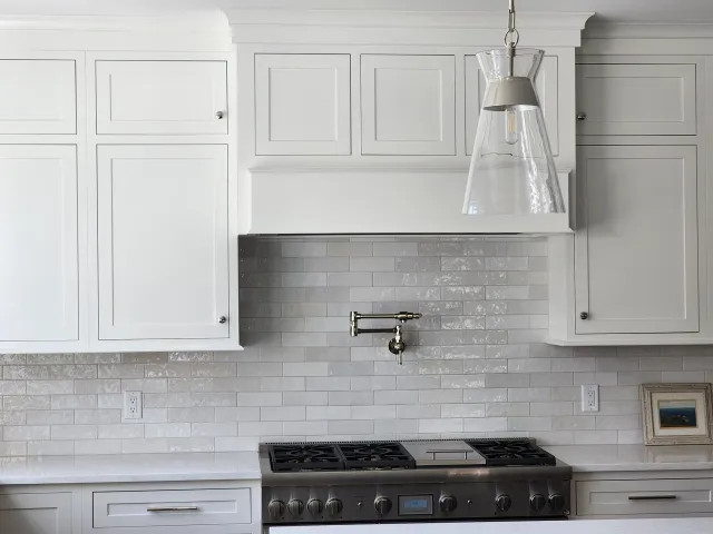 White kitchen backsplash surrounding a range beneath a pendant light