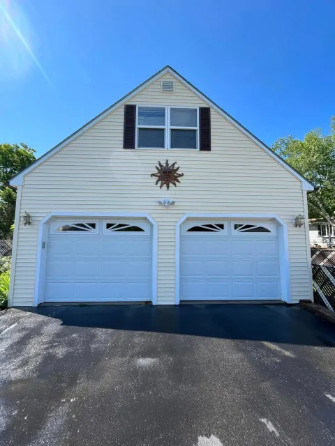 White house with two garage doors, a sunburst decoration, and blue sky overhead.
