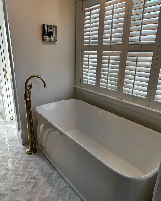 a bathroom with a bathtub and shutters on the windows