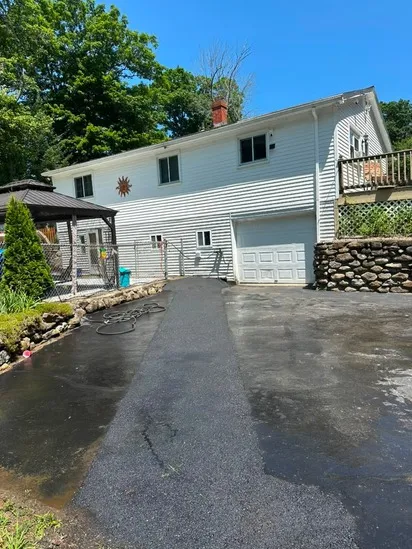 Landscape perspective showcasing a wide section of the asphalt driveway sealcoating leading toward a white residential building and fenced pool area.