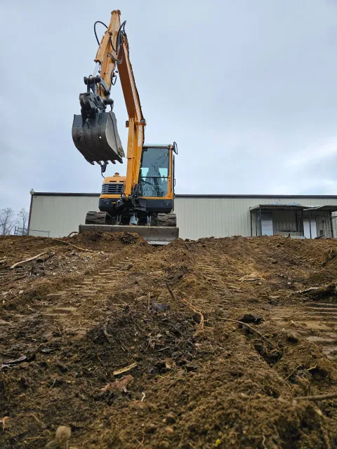 A yellow excavator is digging a pile of dirt in front of a building.