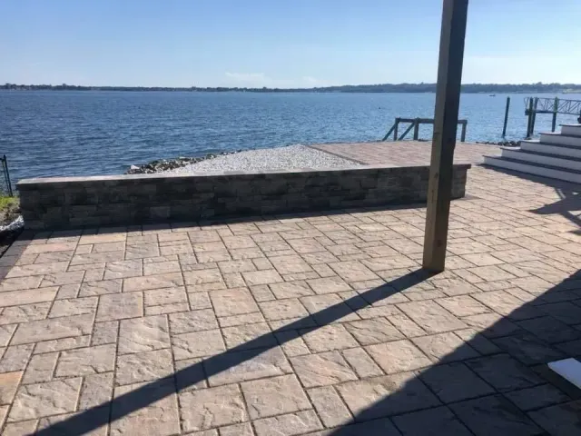 Stone patio overlooking a body of water, with a retaining wall and dock in the distance.